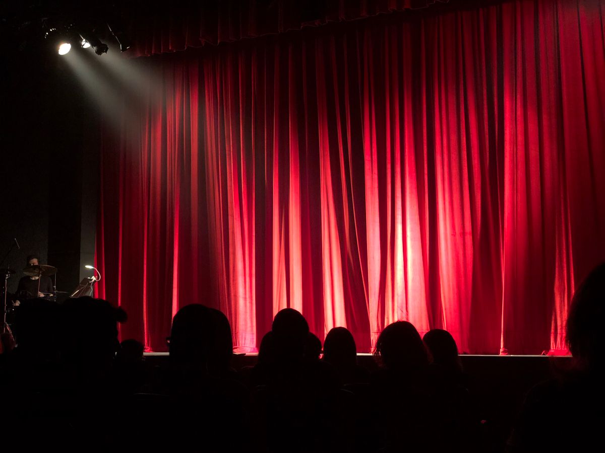 Audience facing a lit theater stage with red curtains
